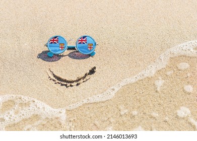 A Painted Smile On The Sand And Sunglasses With The Flag Of Fiji. The Concept Of A Positive And Successful Holiday In The Resort Of Fiji.