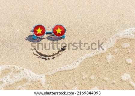 A painted smile on the sand and sunglasses with the flag of the Vietnam. The concept of a positive and successful holiday in the resort of Vietnam.