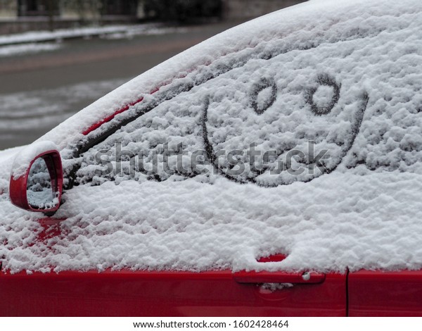 painted\
smiley face in the snow falling on the car\
window