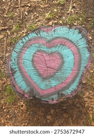 Painted tree stump featuring layered heart art on forest floor