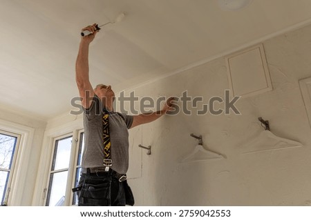Painter applying paint with a roller to a ceiling inside a room.
