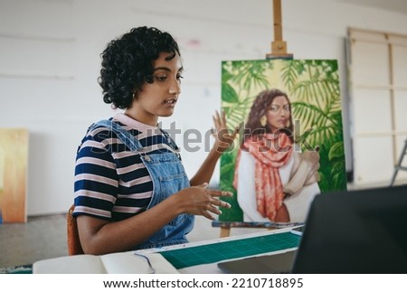 Painter, artist and laptop video call in creative studio for ecommerce sale of canvas painting online. Young indian woman, voip communication chat and designer studying artwork elearning in workshop