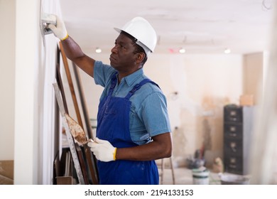 Painter in blue overalls leveling plaster on the wall with a spatula