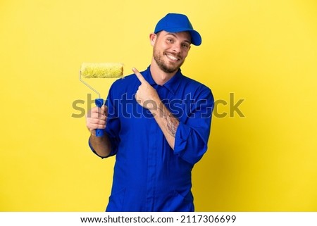 Painter Brazilian man isolated on yellow background pointing to the side to present a product