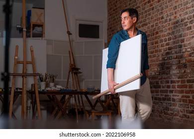 painter Cristian Avilés walking with a canvas under his arm in a painting school - Powered by Shutterstock