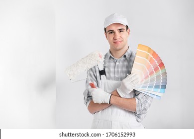 Painter or decorator with handful of colorful paint swatches or color cards holding a roller in his other hand as he smiles at the camera against a white wall