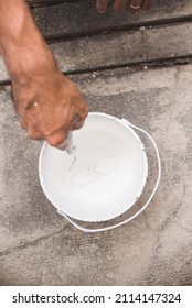 A Painter Dips His Roller Into A White Paint Can. Looking Down, Top View. Construction Or Home Renovation.