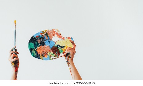 Painter equipment. Drawing tools. Woman artist hands holding colorful messy palette and paintbrush isolated on white empty space background.