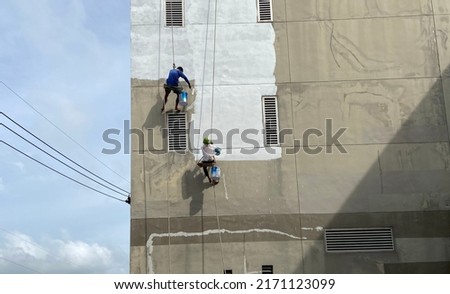 painter fixing the wall and painting on the wall of the building Construction worker with a roller brush work on tall buildings without safety equipment The concept of dangerous work at heights