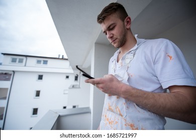 Painter making telephone call while standing on balcony during break from work  Decorator Using Mobile Phone Standing Outside