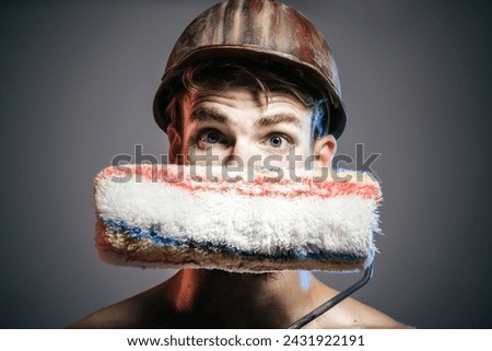 Painter man. Closeup portrait of painter, designer or builder with paint roller. Professional painter in hard hat with painting roller. Repair, room painting job - painter in helmet with paintroller.