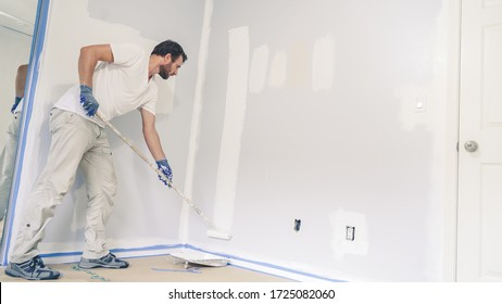 Maler malt die Wand zu Hause, mit Malwalze und weißer Farbe. Zimmerrenovierungen zu Hause.