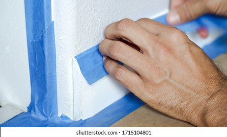 Malermann, der das blaue Band mit Masking benutzt, um Baseboard zu sichern, zu formen. Vorbereitung für die Zimmermalerei.