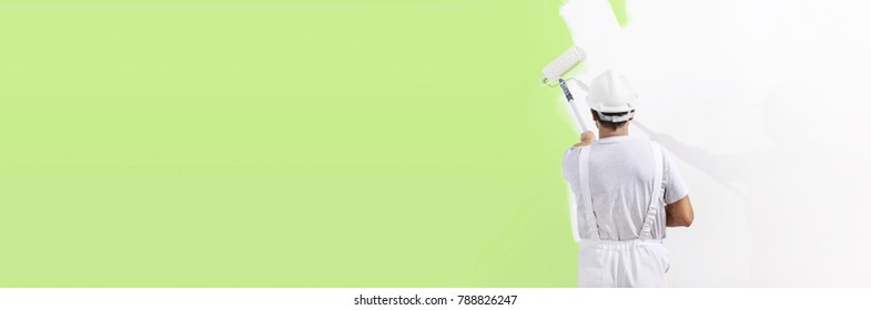 painter man at work with a paint roller, wall painting green color ecological concept, web banner template