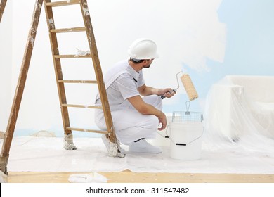 painter man at work takes the color with paint roller from the bucket