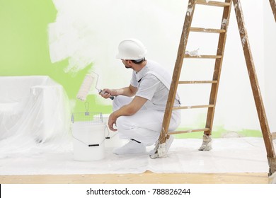 Maler bei der Arbeit nimmt die Farbe mit der Farbwalze aus dem Eimer