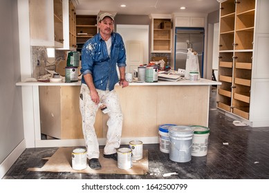 Painter In Messy Clothes Holding Wet Paintbrush, Standing In Home Kitchen Remodel Fixer Upper Project, Dripping Paint Cans Everywhere, Cabinets Open