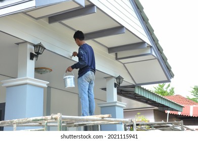 a painter one hand carry color bucket and other hand hold brush standing on scaffolding,painting house gable.worker man paint exterior house wall,people work at construction,maintenance or repair home - Shutterstock ID 2021115941