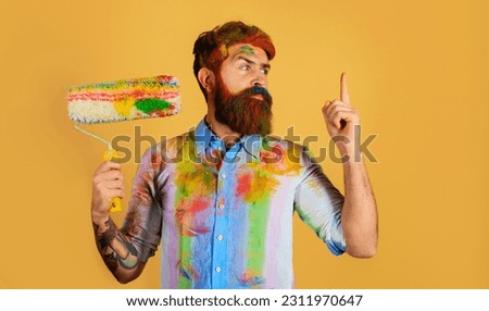 Painter with paint roller pointing finger up. Professional painter, decorator, builder worker with paintroller. Bearded worker with paint roller. Repairman or handyman in dye shirt with paint roller.