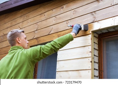 painter with paintbrush painting house wood facade