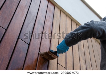 Painter with paintbrush painting house wood facade with protective oil, low angle perspective view
