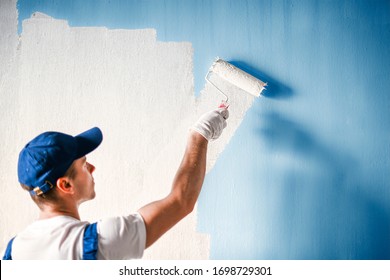 Painter painting a wall with paint roller. Builder worker painting surface with white color.