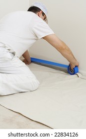 Painter Protecting The Trim With Blue Masking Tape