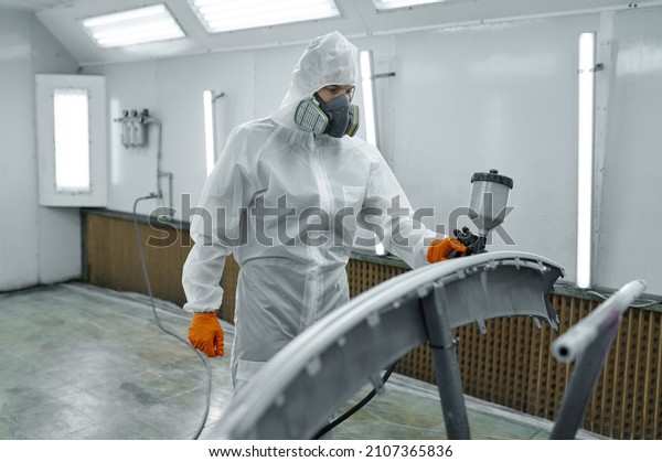 Painter in\
protective mask painting automobile\
part