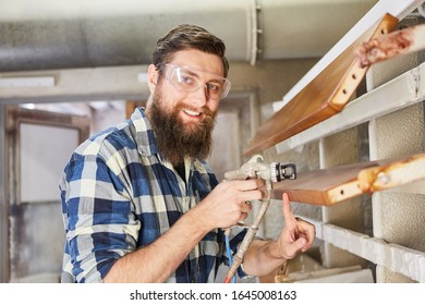 Painter Smiling While Painting Furniture With Spray Gun In Carpentry