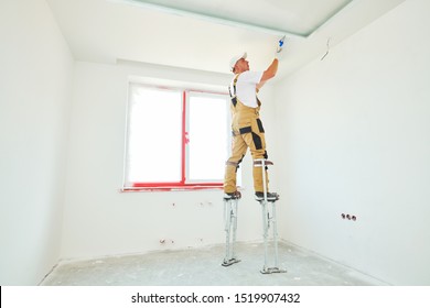 Painter In Stilts With Putty Knife. Plasterer Smoothing Ceiling Surface At Home Renewal