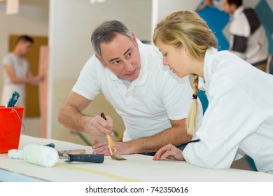 painter teaching paintbrush technique to apprentice