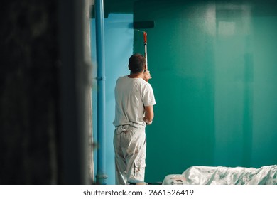 Painter is using a paint roller to apply green paint to a wall, showcasing a home improvement project