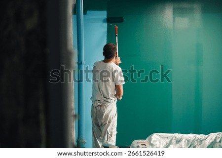 Painter is using a paint roller to apply green paint to a wall, showcasing a home improvement project