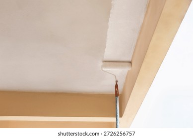 Painter using a roller to apply fresh white paint to a ceiling.