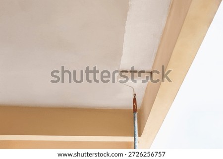 Painter using a roller to apply fresh white paint to a ceiling.