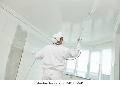 Malerarbeiter mit luftloslackierendem Spritzspritzer, Deckendecke auf Weiß