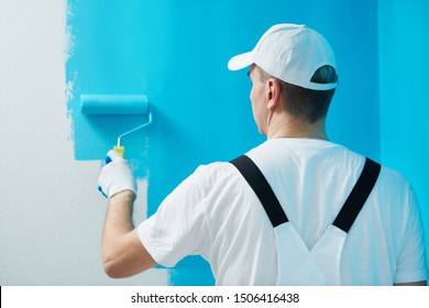 Painter worker with roller painting wall surface into color