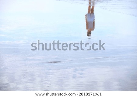 Painterly reflection of a person walking on wet sand as receding sea water creates a mirror effect on the beach with copy space