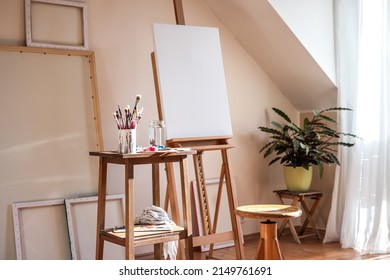 Painting art studio at loft apartment. Empty cozy workplace. Clear canvas on easel and paintbrush on table - Powered by Shutterstock