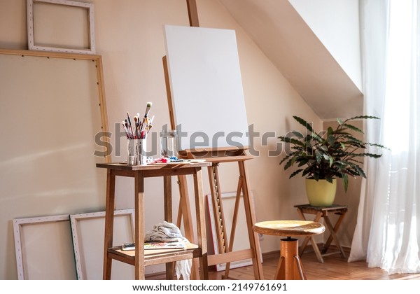 Painting art studio at loft\
apartment. Empty cozy workplace. Clear canvas on easel and\
paintbrush on table