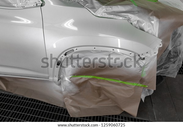 Painting the car body\
parts of the driver\'s door and the white wing in the spray booth in\
the body repair shop; other elements are covered with film and\
paper from splashing.