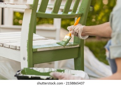 Painting Chair with brush in protective gloves. Worker paints garden furniture green. Renewing, Renovation Wooden Garden Furniture - Shutterstock ID 2158865437