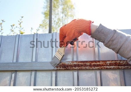 Painting the fence. Woman's hand painting steel fence with a brush