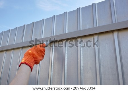 Painting the fence. Woman's hand painting steel fence with a brush