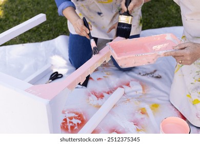 Painting furniture outdoors, two people using brushes and pink paint. DIY, home improvement, teamwork, creativity, renovation - Powered by Shutterstock