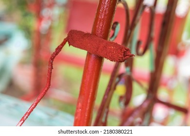 Painting The Grilles Of An Old Glider Swing Made Of Wrought Iron With Red Oxide Primer Paint. Using A Small Paint Roller. Restoring Or Rebuilding Outdoor Furniture Or Playground Equipment.