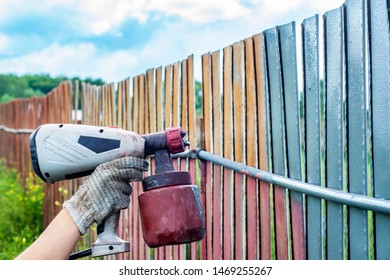 Painting Metal Fence Spray. Man Paints A Fence With A Paint Sprayer