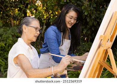 Painting on canvas, Asian granddaughter and grandmother enjoying outdoor art activity together. Creativity, friendship, leisure, bonding, hobby, nature - Powered by Shutterstock