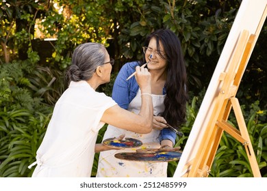 Painting on canvas, Asian granddaughter and grandmother enjoying outdoor art activity together. family,  creativity, outdoors, leisure, bonding, hobby, friendship - Powered by Shutterstock