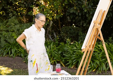 Painting on canvas, elderly asian woman in apron focusing on her artwork outdoors. creativity, artist, concentration, hobby - Powered by Shutterstock